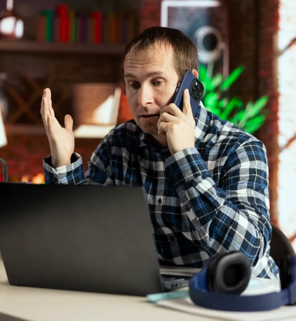 Kierownik serwisu rozmawia przez telefon przy laptopie, próbując opanować problemy z organizacją zleceń